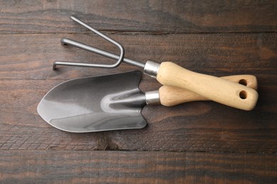 Gardening trowel and rake on wooden table, top view