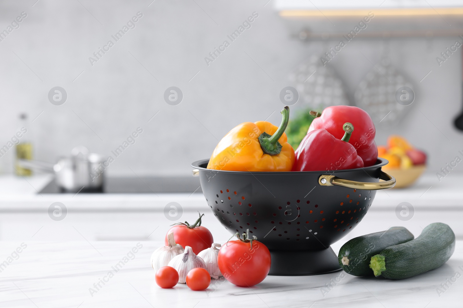 Photo of Black colander and different vegetables on white marble table in kitchen. Space for text