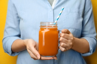 Woman holding mason jar of tasty carrot juice, closeup