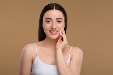 Beautiful woman removing makeup with cotton pad on beige background