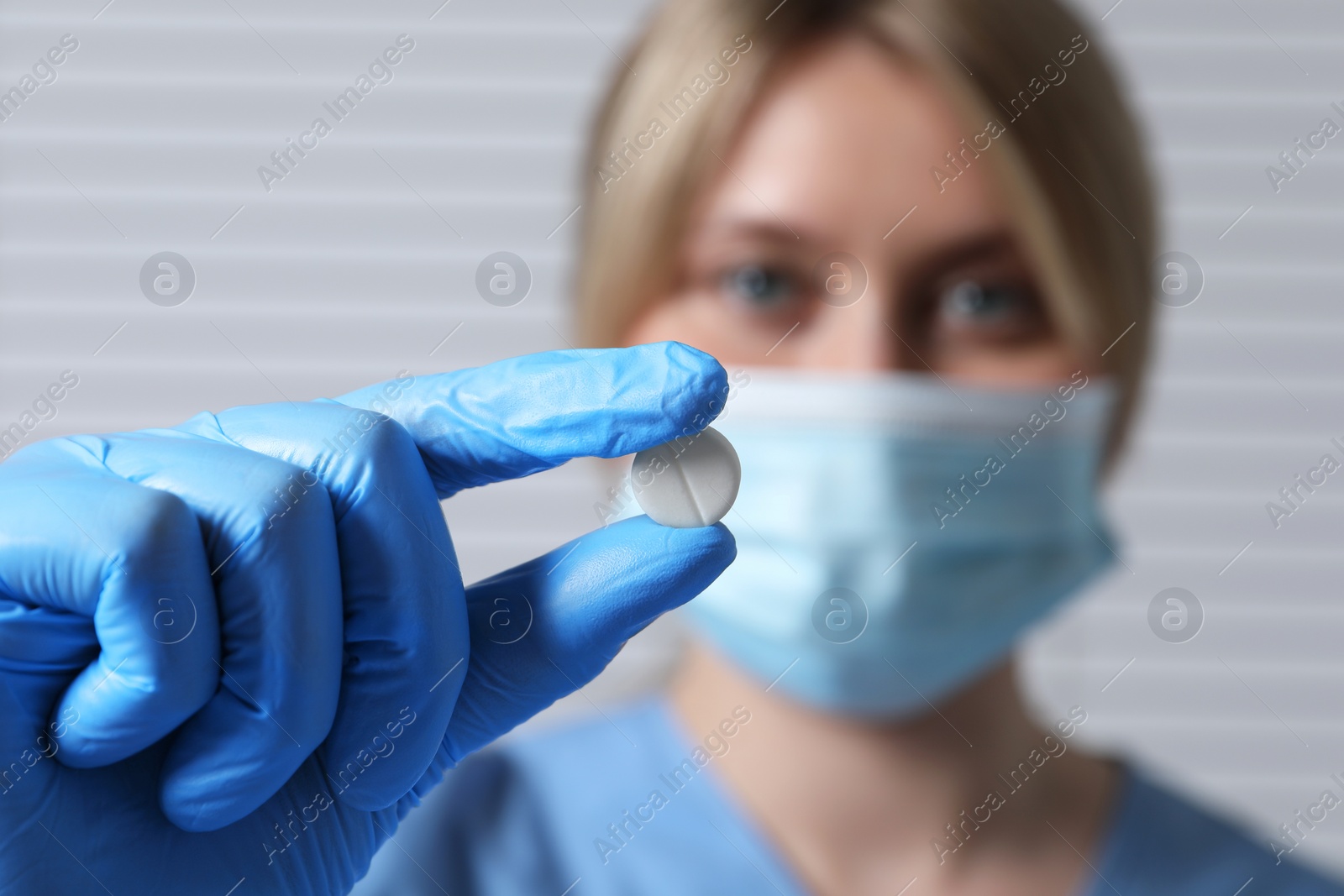 Photo of Doctor holding pill on light background, selective focus