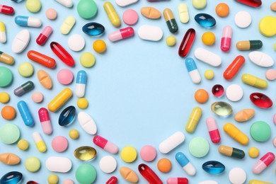 Photo of Frame made of many different pills on light blue background, flat lay. Space for text