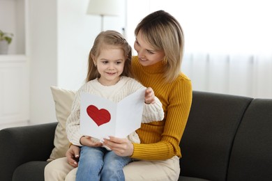 Photo of Little daughter congratulating her mom with greeting card at home. Happy Mother's Day