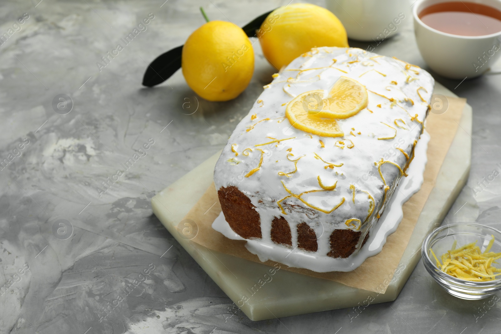 Photo of Tasty lemon cake with glaze, citrus fruits and zest on gray textured table, closeup. Space for text
