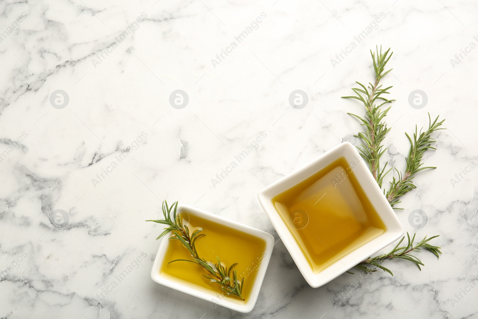 Photo of Square bowls of rosemary oil on light background, top view