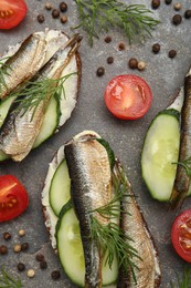 Photo of Delicious sandwiches with sprats, cucumber and dill served on grey table, flat lay