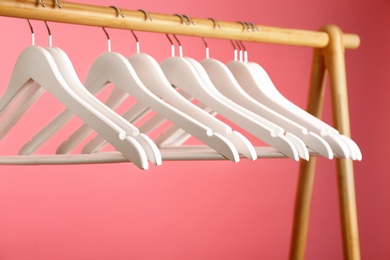Photo of Empty clothes hangers on wooden rack against color background