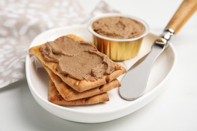 Photo of Crispy crackers with delicious meat pate and knife on white table, closeup