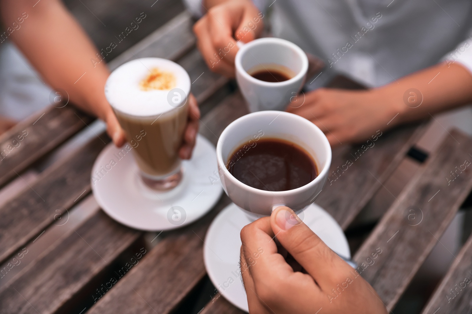 Photo of Friends drinking coffee at wooden table in outdoor cafe, closeup