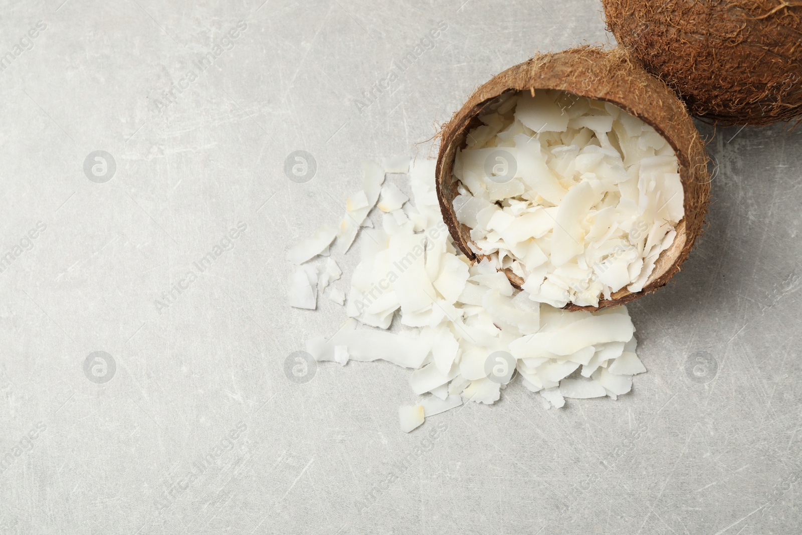 Photo of Tasty coconut chips and shell on grey table, above view. Space for text