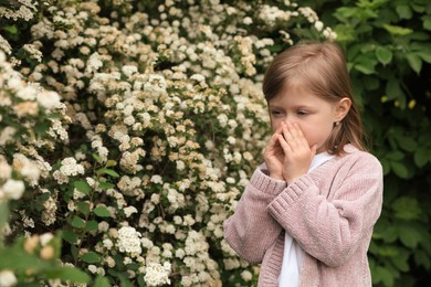 Photo of Little girl suffering from seasonal pollen allergy near blossoming tree on spring day