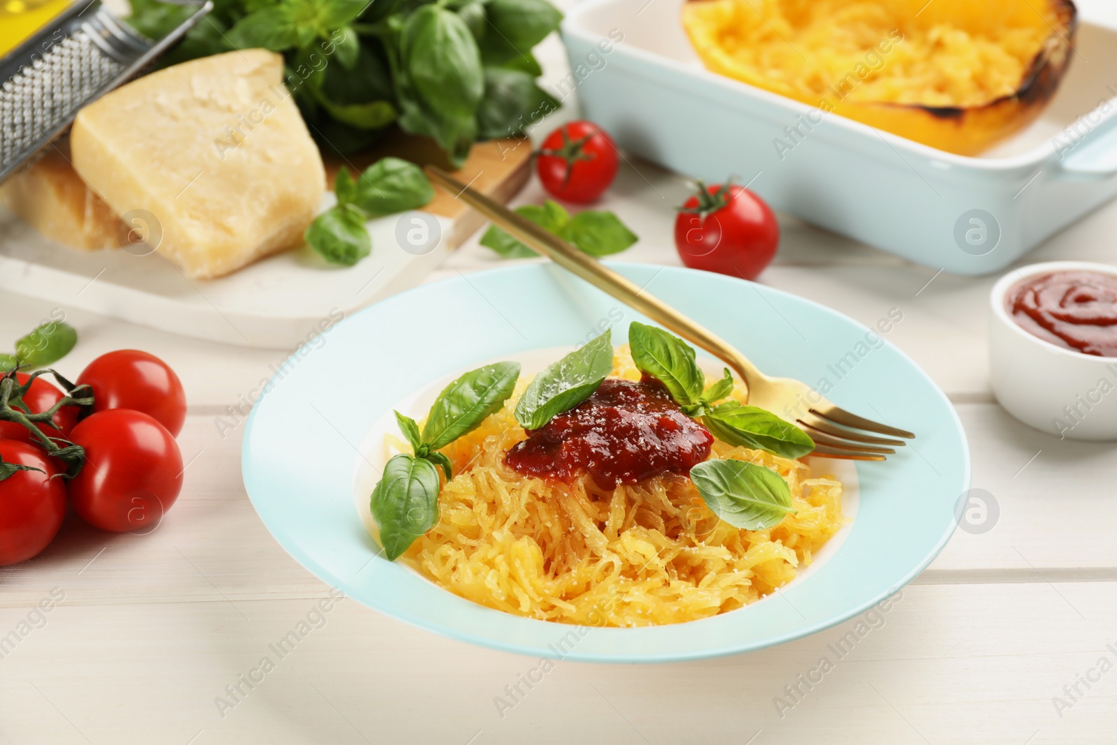 Photo of Tasty spaghetti squash with tomato sauce, cheese and basil served on white wooden table