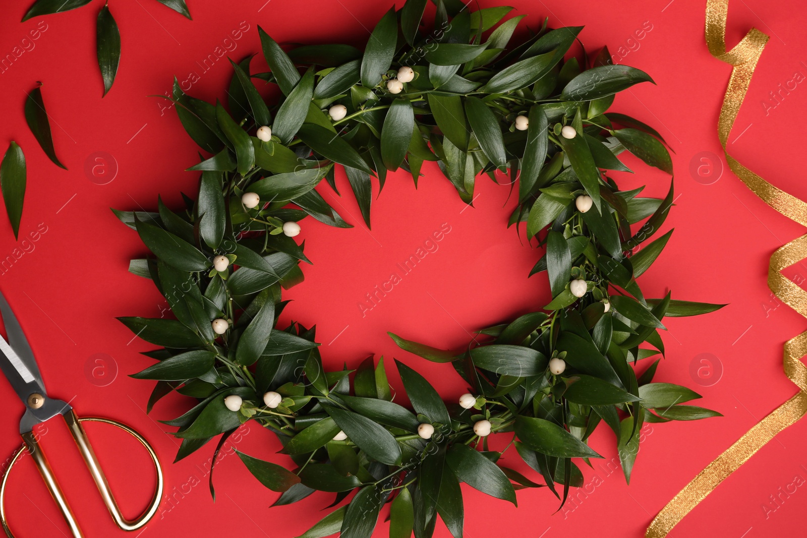 Photo of Beautiful handmade mistletoe wreath and florist supplies on red background, flat lay. Traditional Christmas decor