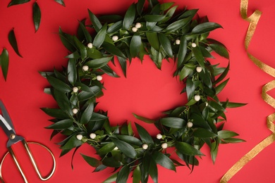 Photo of Beautiful handmade mistletoe wreath and florist supplies on red background, flat lay. Traditional Christmas decor