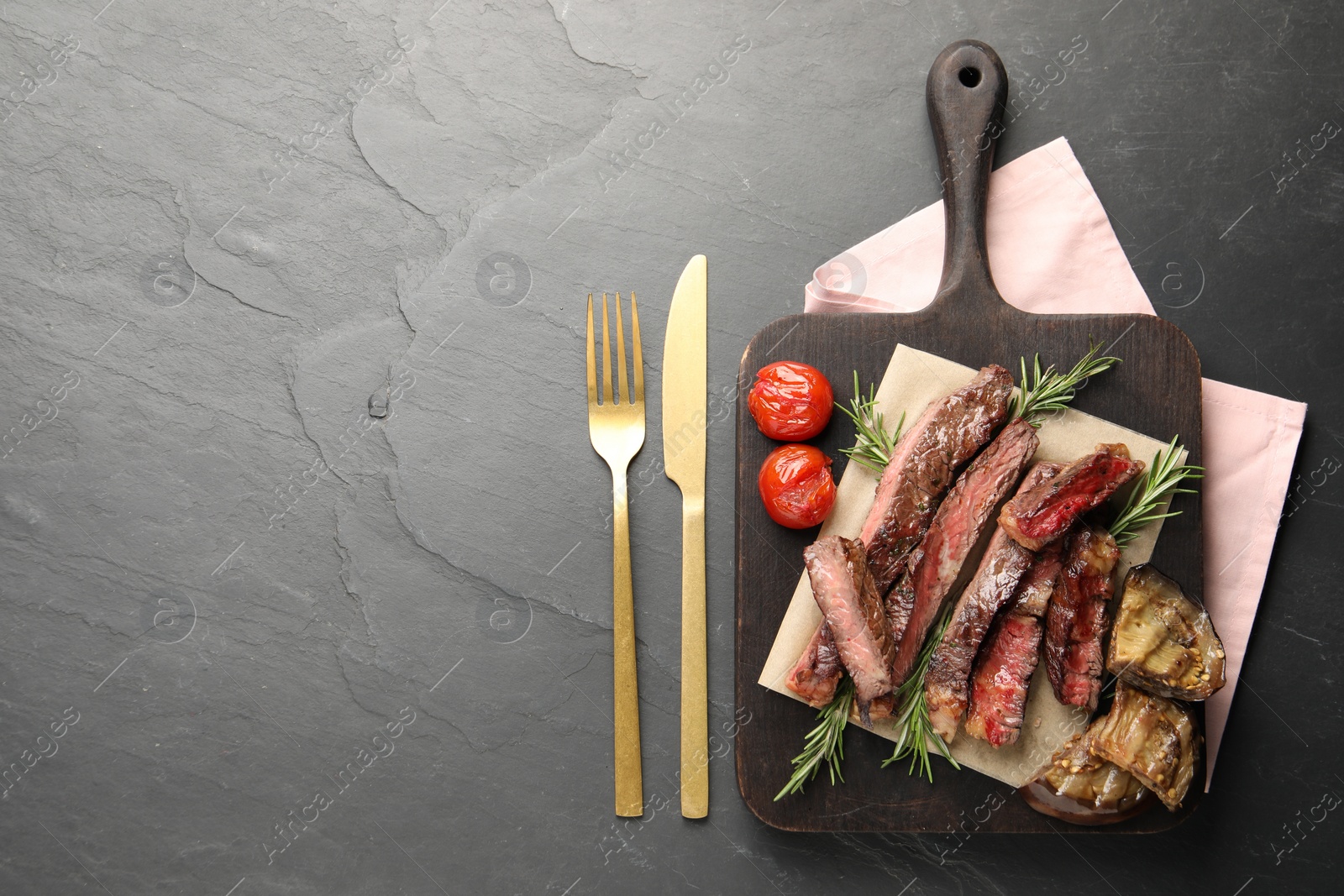 Photo of Delicious grilled beef with vegetables and rosemary served on dark gray table, top view. Space for text