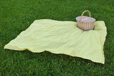 Photo of Picnic basket with checkered tablecloth on green grass outdoors