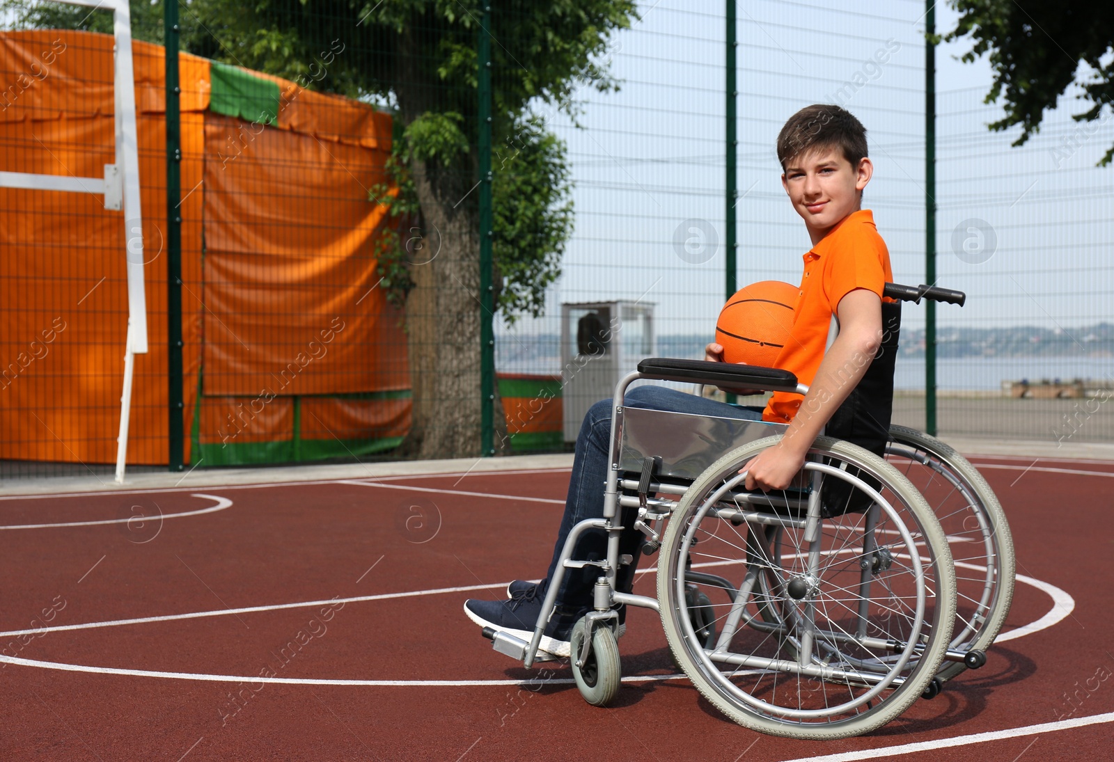 Photo of Disabled teenage boy in wheelchair with basketball ball at outdoor court