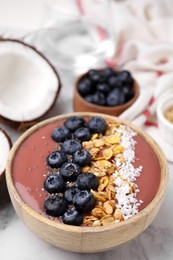 Photo of Bowl of delicious fruit smoothie with fresh blueberries, granola and coconut flakes on white marble table
