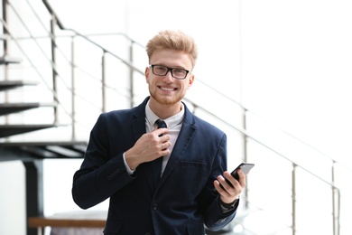 Photo of Portrait of handsome young man in elegant suit with glasses and smartphone indoors