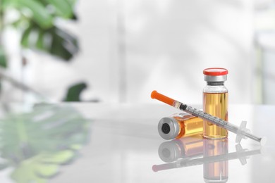 Photo of Glass vials and syringe with orange medication on white table. Space for text