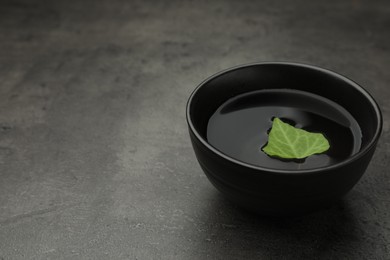 Black bowl with water and green leaf on grey table. Space for text