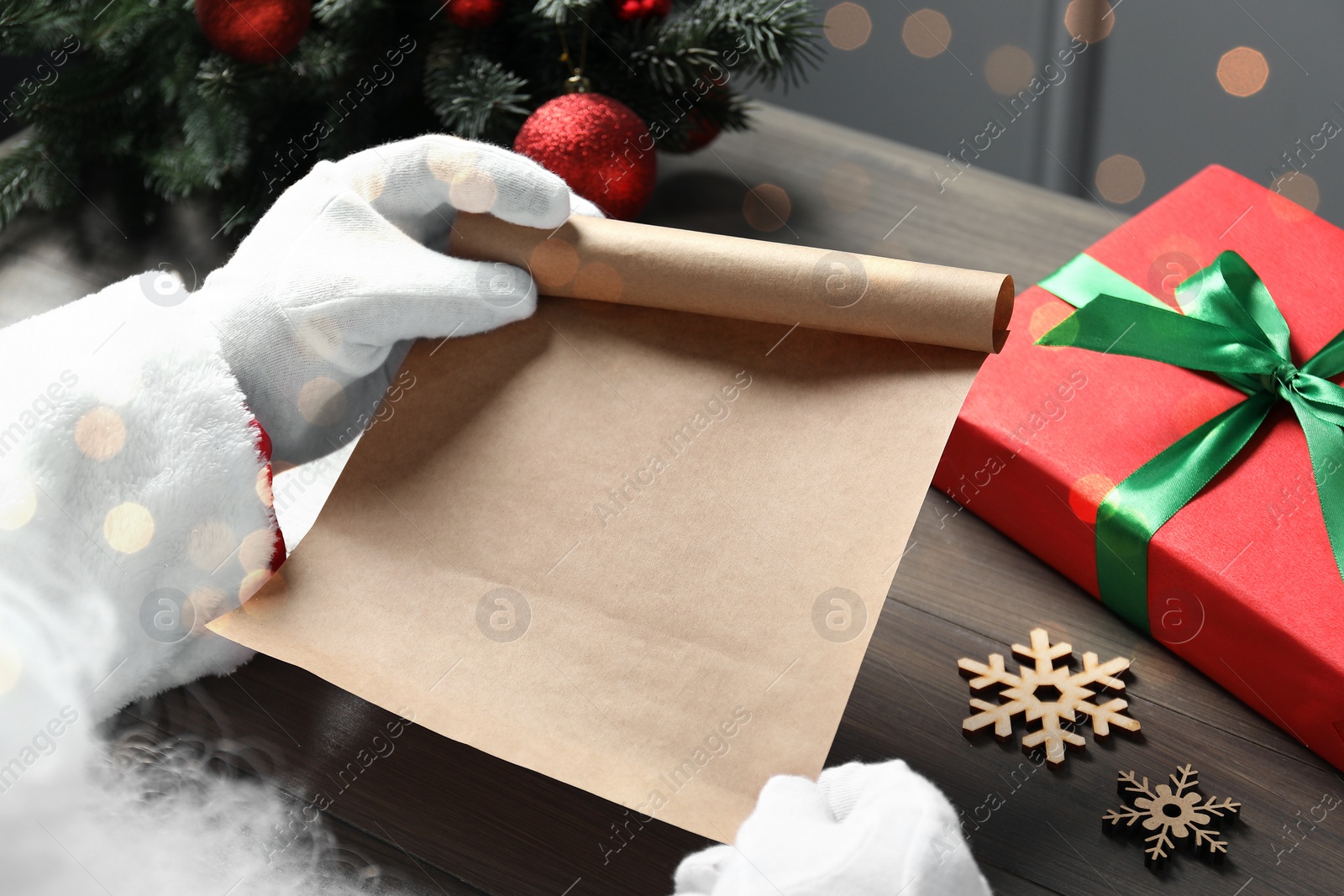 Photo of Santa Claus with letter, gift box and Christmas decor at wooden table, closeup. Space for text