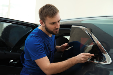 Worker tinting car window with foil in workshop