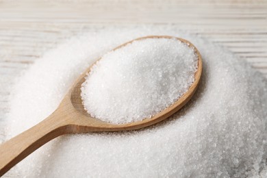 Photo of Spoon with granulated sugar on white wooden table, closeup