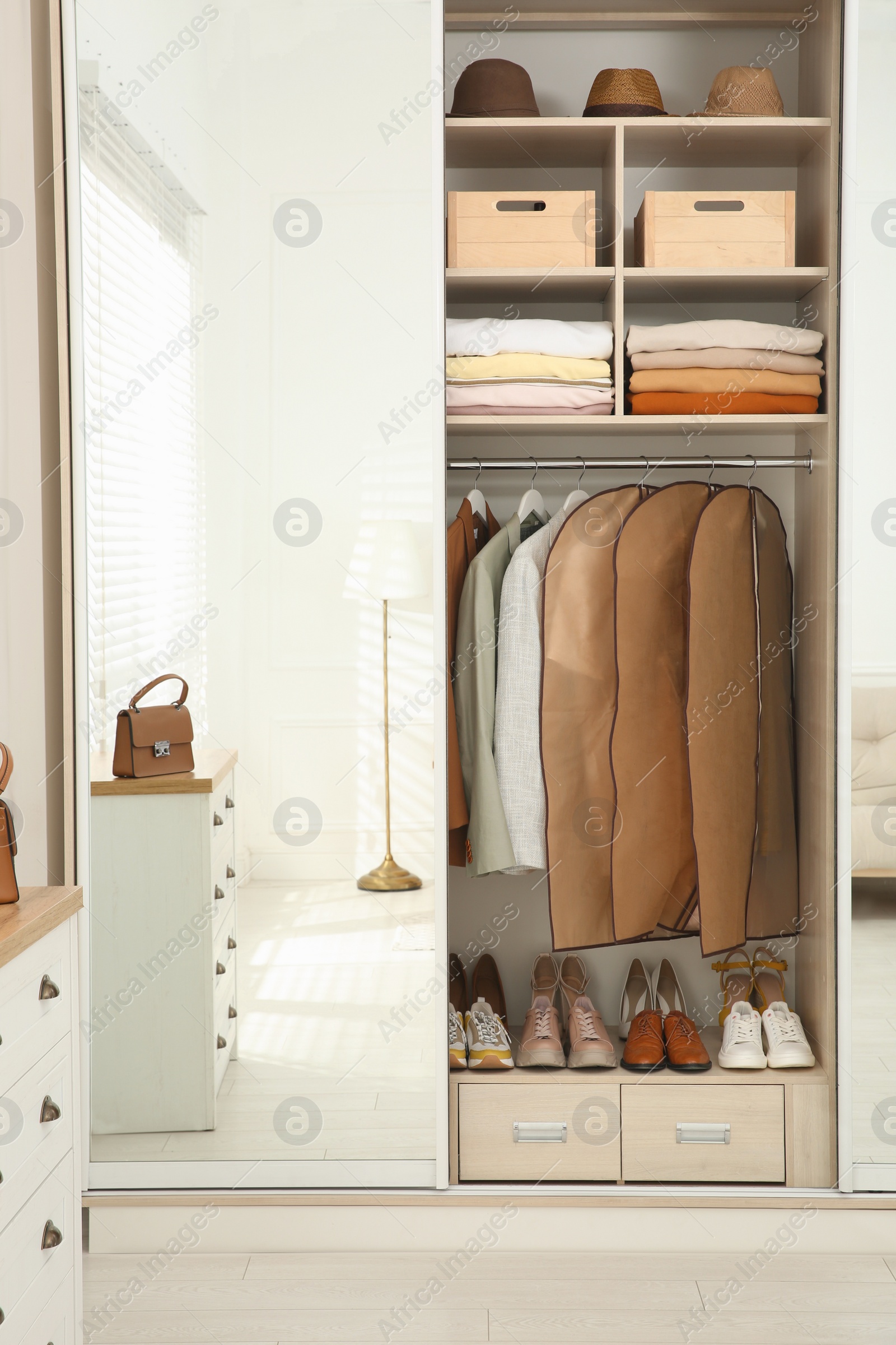 Photo of Garment bags with clothes on rack in wardrobe indoors