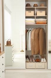 Garment bags with clothes on rack in wardrobe indoors