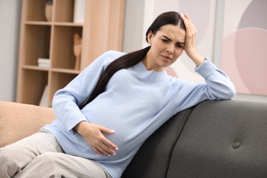 Pregnant woman suffering from headache on sofa at home