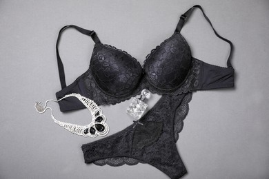 Photo of Elegant black women's underwear, perfume and necklace on grey background, flat lay