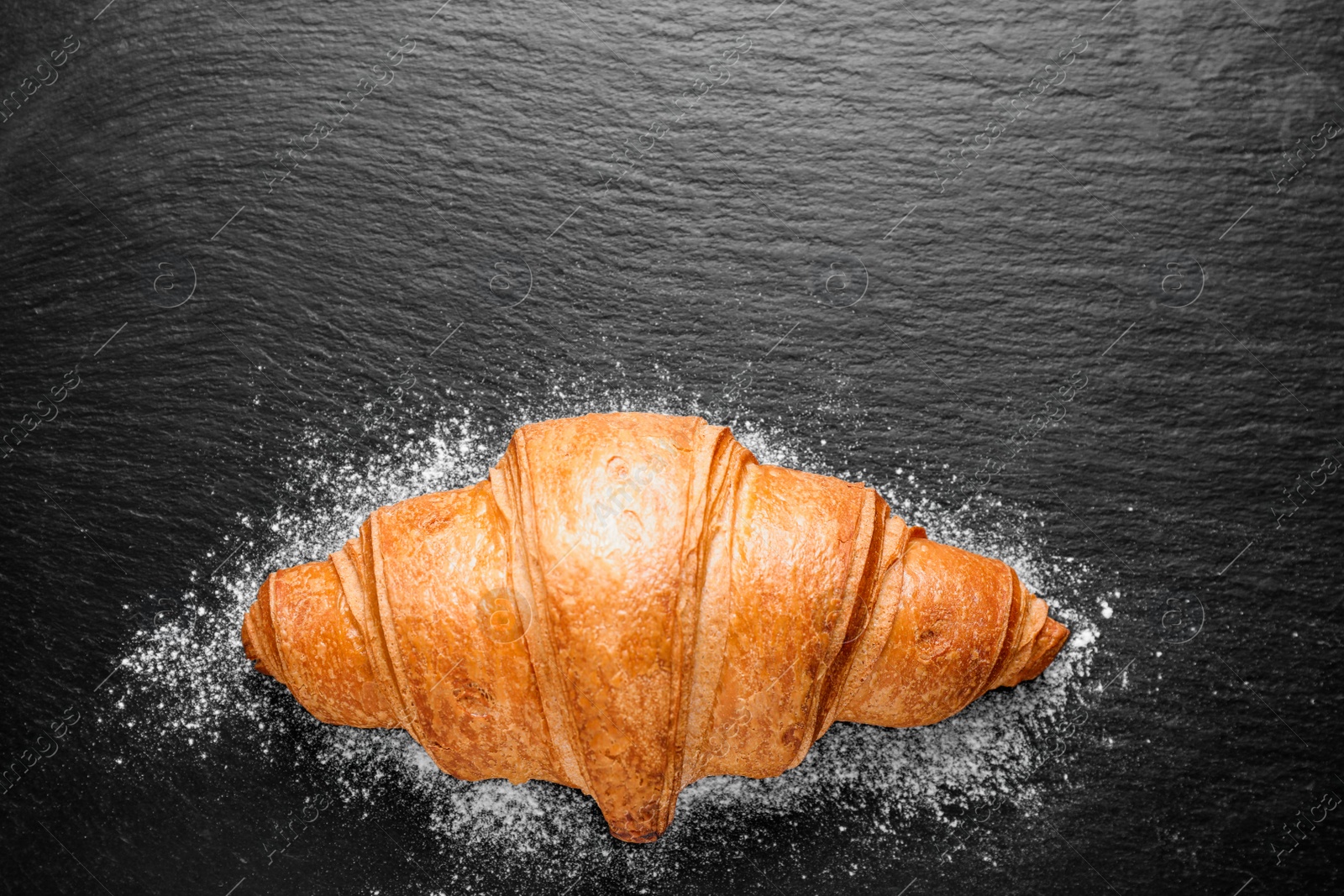 Photo of Tasty fresh croissant on black table, top view