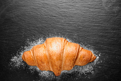 Tasty fresh croissant on black table, top view