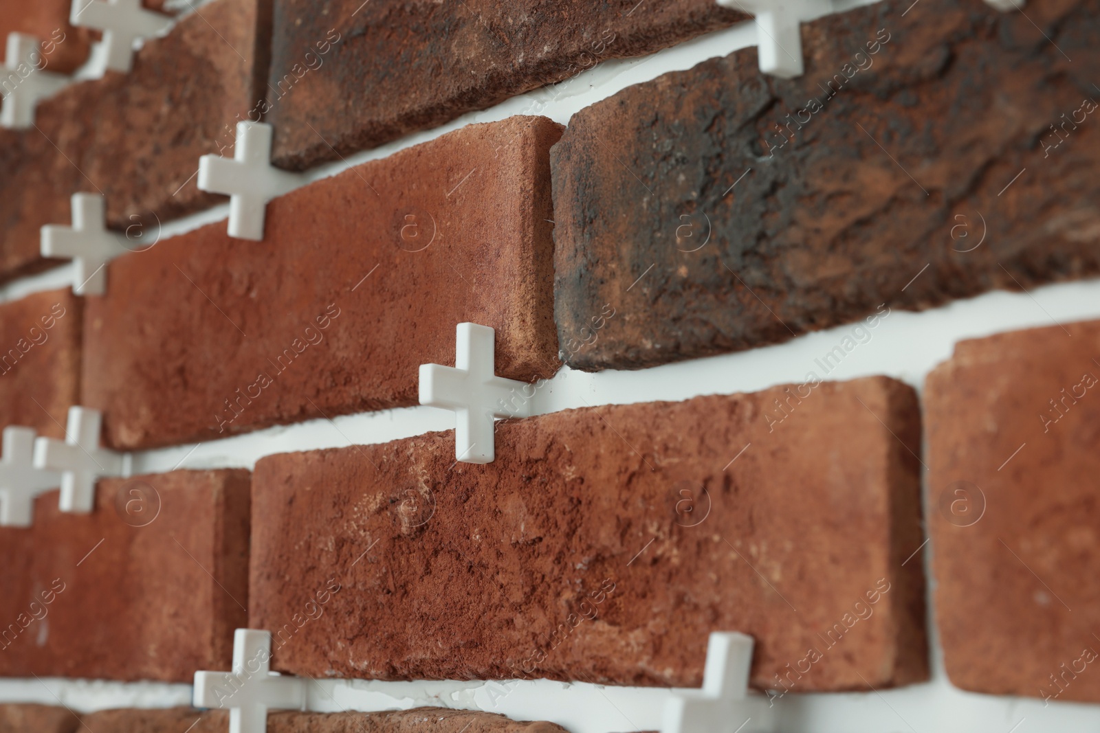 Photo of Decorative bricks with tile leveling system on wall, closeup