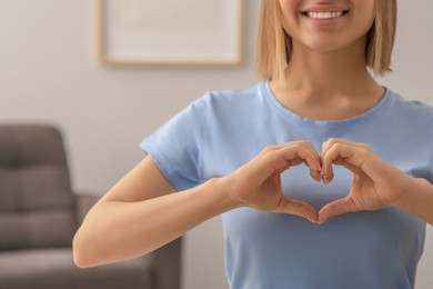 Young woman making heart with hands indoors, closeup. Volunteer concept