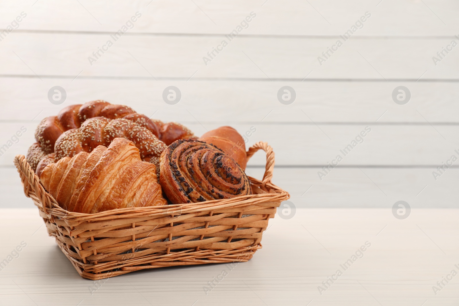 Photo of Wicker basket with different tasty freshly baked pastries on white table, space for text