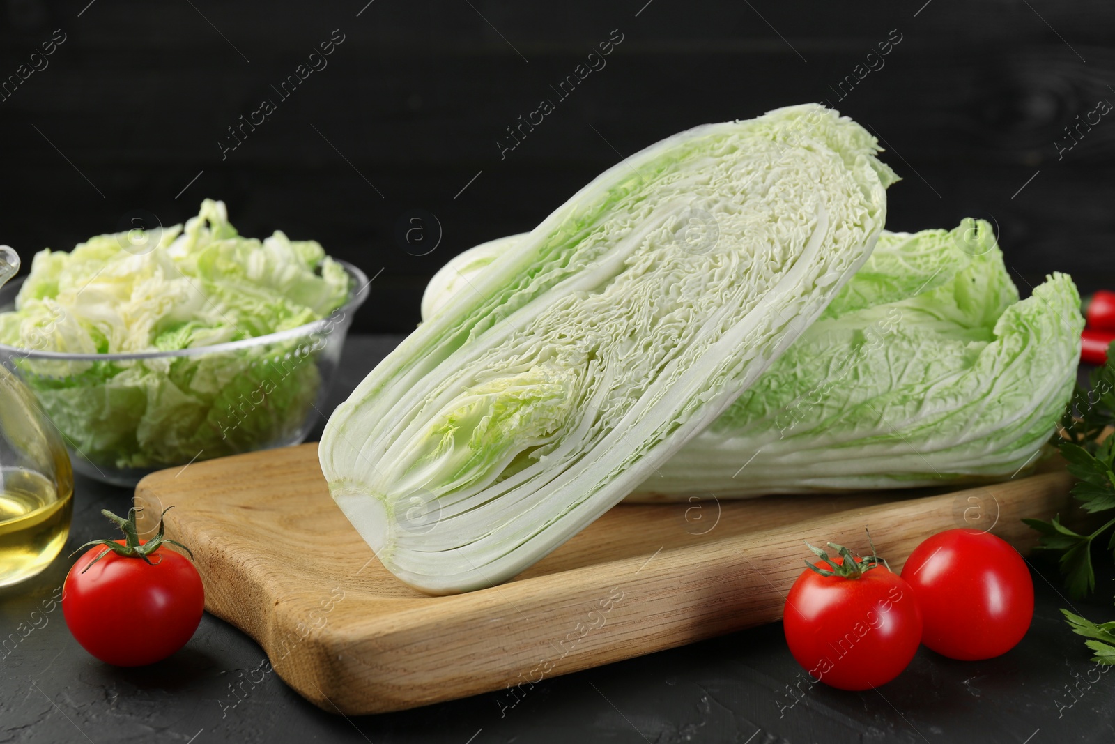 Photo of Fresh Chinese cabbages, tomatoes and oil on black textured table