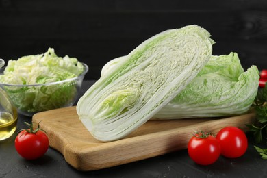 Photo of Fresh Chinese cabbages, tomatoes and oil on black textured table