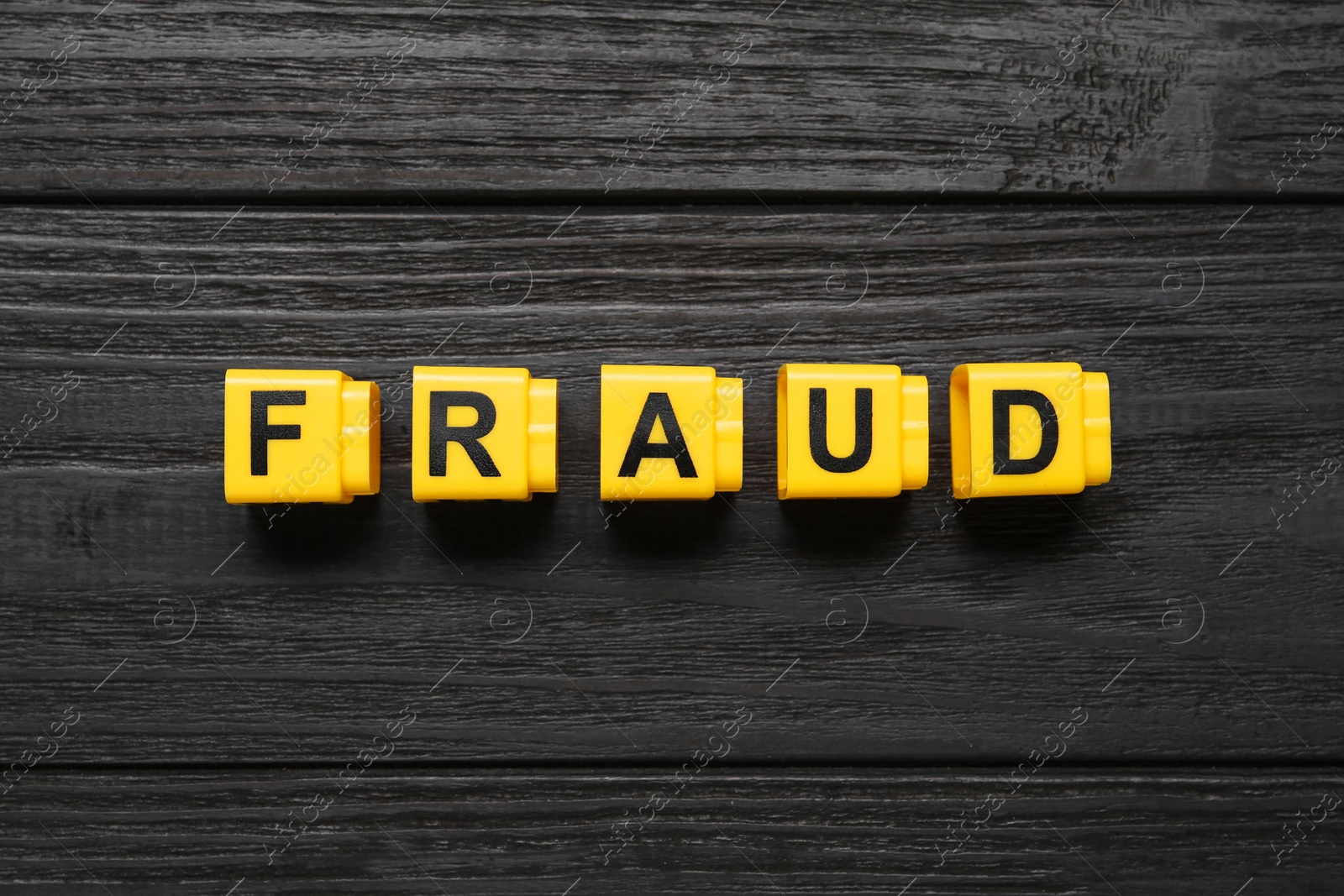 Photo of Word Fraud of yellow cubes with letters on black wooden background, flat lay