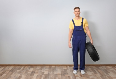 Male mechanic with car tire on light wall background