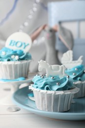 Photo of Delicious cupcakes with light blue cream and toppers for baby shower on white wooden table