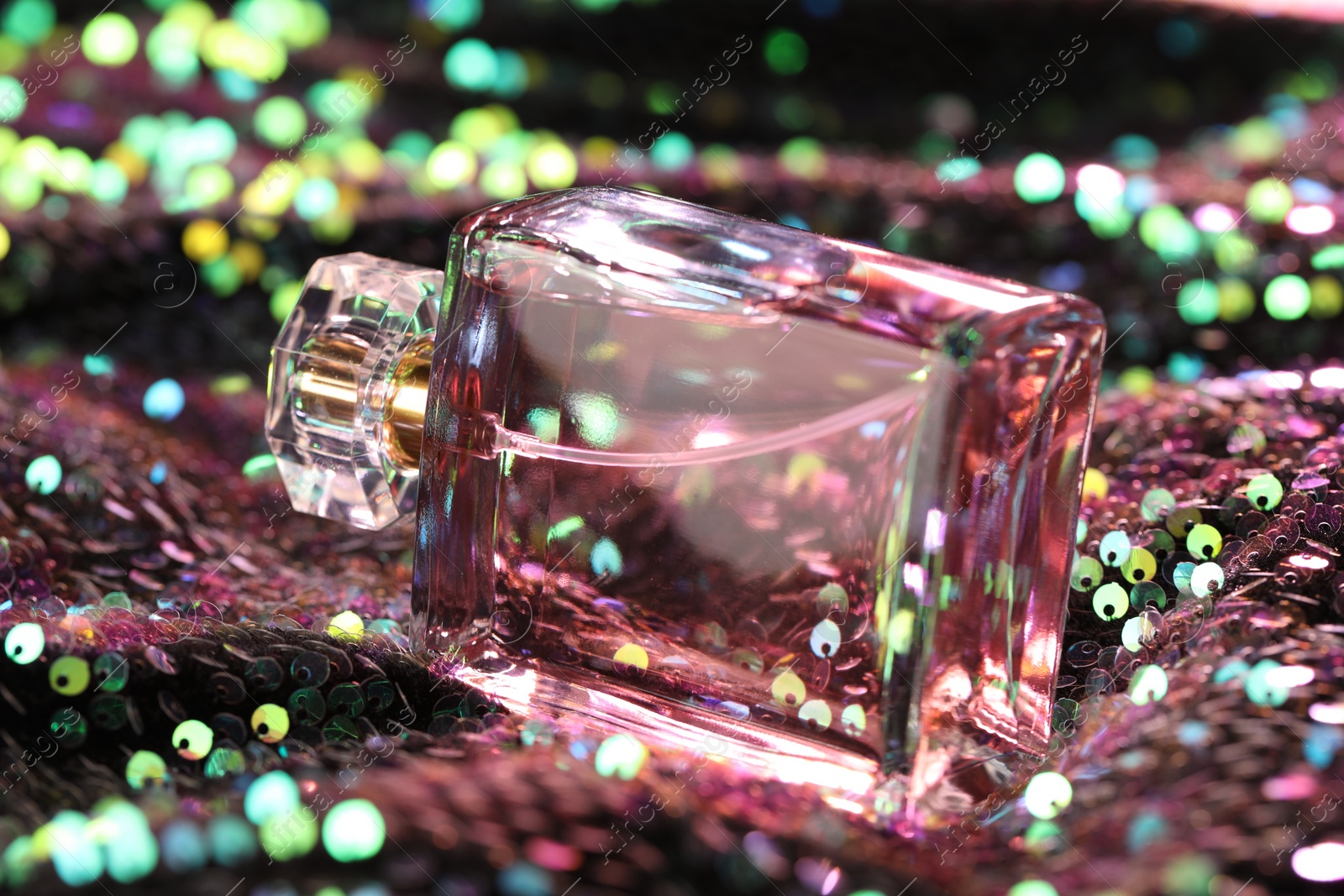 Photo of Luxury perfume in bottle on fabric with colorful sequins, closeup