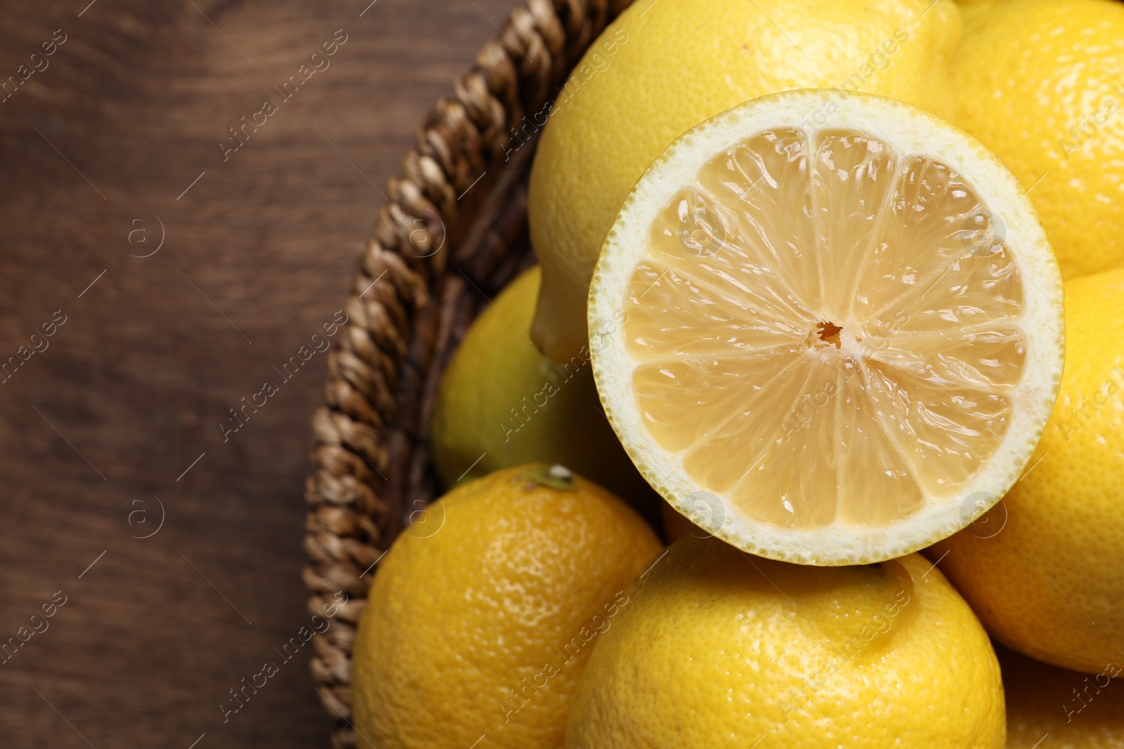 Photo of Fresh lemons in wicker basket on wooden table, closeup