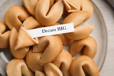 Tasty fortune cookies with prediction Dream BIG in plate on wooden table, top view