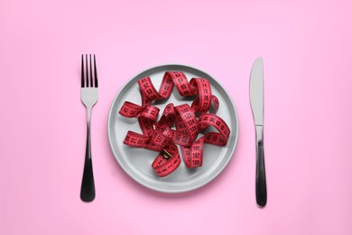 Measuring tape, fork and knife on pink background, flat lay. Weight loss concept
