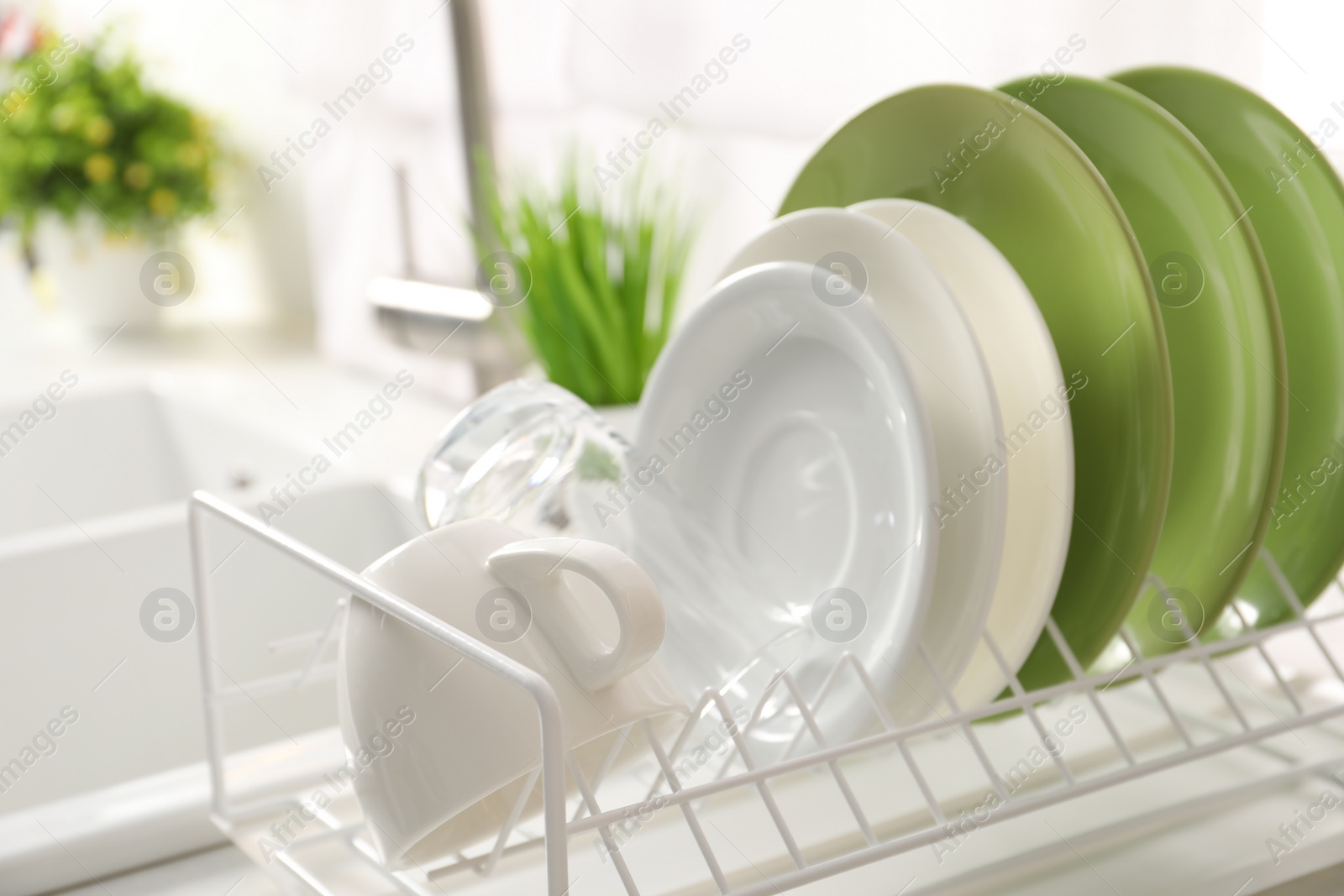 Photo of Drainer with different clean dishware, glass and cup indoors, closeup