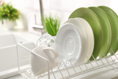 Photo of Drainer with different clean dishware, glass and cup indoors, closeup