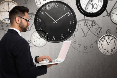 Image of Time management concept. Businessman working on laptop surrounded by clocks