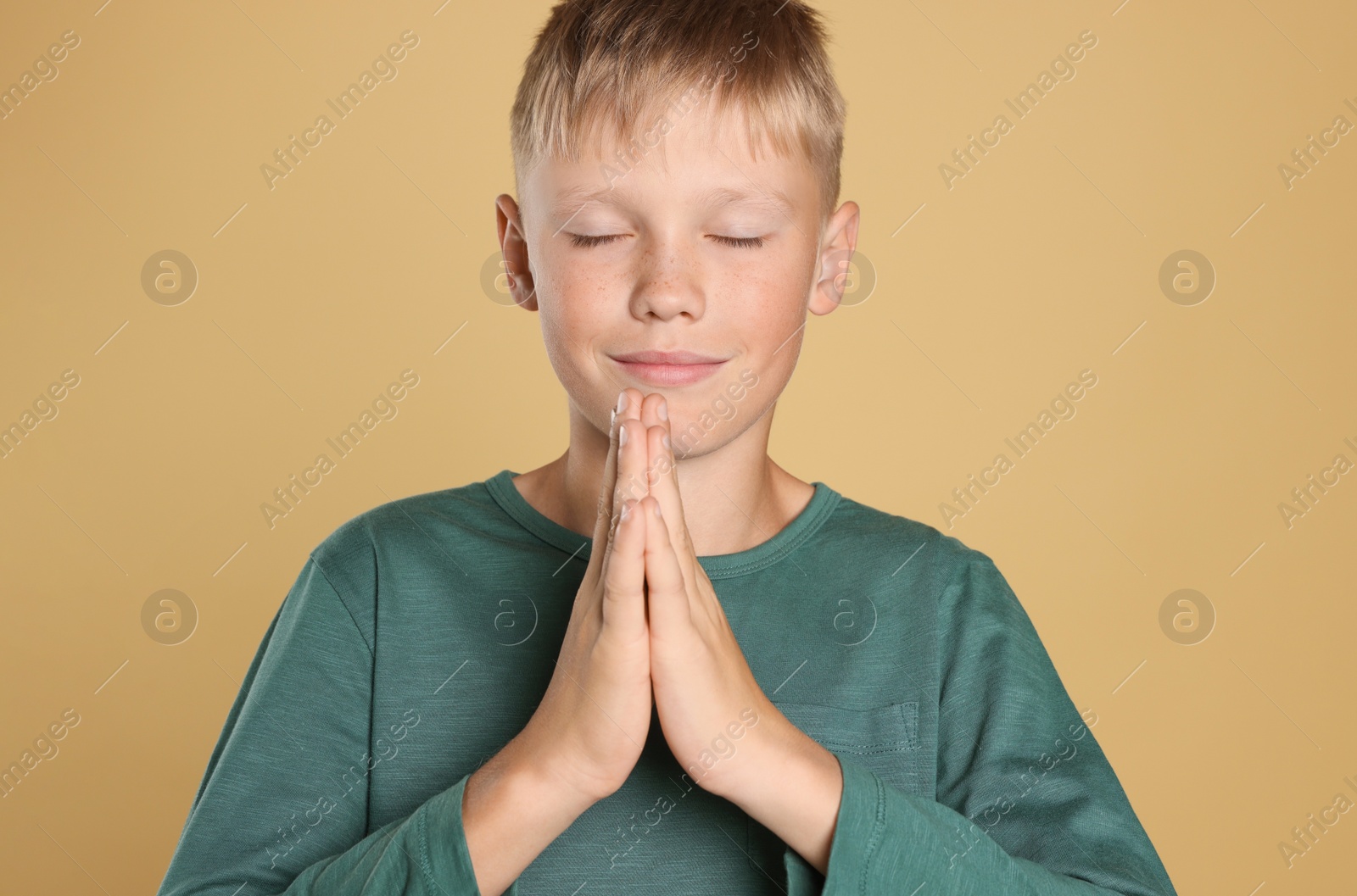 Photo of Boy with clasped hands praying on beige background